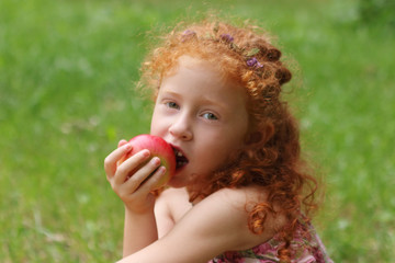 Little girl eats apple on lawn in green summer park, close up, s