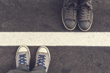 Two pair of sneakers on a asphapt road. - obrazy, fototapety, plakaty