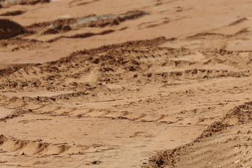 Yellow sand with many tractor tracks on construction site at sun