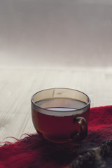 A Cup of hot tea is on the warm scarf on the background of wooden boards, comfort, rest, relaxation, holidays, vacation