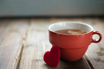 On old vintage boards is a red Cup with tea and lemon, next to the fabric heart behind the rose petals toned