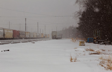 back view of Freight train running on the railway tracks in winter while is snowing