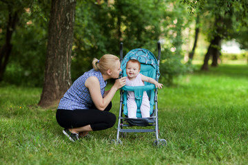 Fototapeta premium Mum holds on hands of a small baby near the bushes , the kid touches the foliage , autumn in the park in the summer on the nature