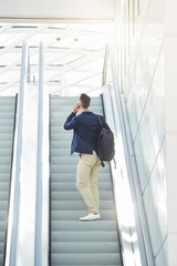 business man from behind standing on escalator on phone call