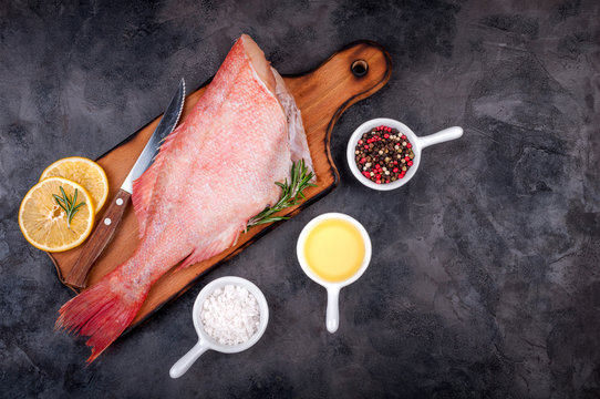 Fresh fish raw snapper with lemon slices, herbs rosemary, salt and pepper on dark stone background. Healthy food and diet concept, top view, copy space. Ingredients for cooking fish