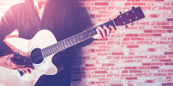 A man playing guitar on brick wall with croped image