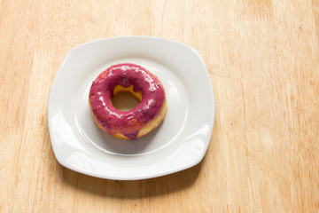 Donut with blueburry topping in white plate on wooden background