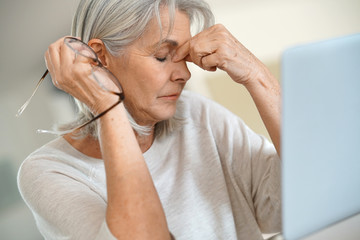 Senior woman in front of laptop, having a headache