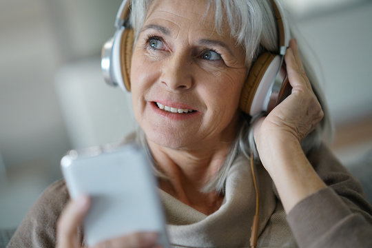 Senior woman at home listening to music with smartphone
