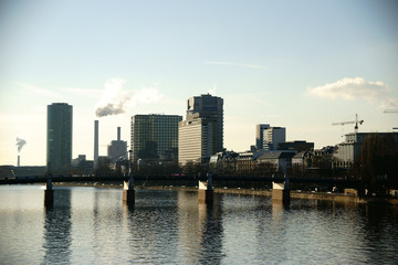 Fototapeta na wymiar Hochhäuser an der Friedensbrücke Frankfurt / Hochhäuser wie der Westhafen Tower sowie Industrie an der Friedensbrücke und entlang des Flusses Main in Frankfurt.