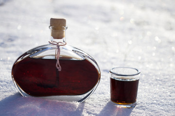 walnut liqueur in the snow. bottle and shot glass in the frosty sunny winter day.  snorter of homemade alcohol 