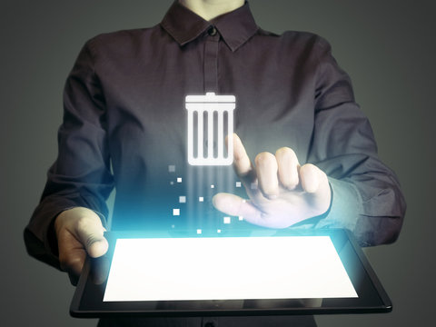 Image of a girl with tablet in her hands. She presses trash can icon. The concept of deleting files, contacts, putting in order, cleaning service etc