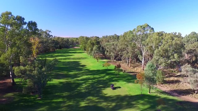 Aerial view of Golfers in electric Golf Buggy with Caddy driving through bush land Golf Course by river.