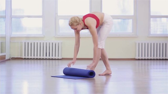 Young fit woman practicing yoga asana or pose. Young woman working out in gym, she unwraps the mat before starting yoga in gym class.