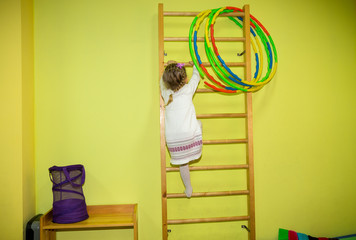 Little girl kid climbs the stairs on sports equipment in kindergarten. Wall bars. Children's sports. Healthy lifestyle from childhood