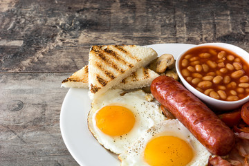 Traditional full English breakfast with fried eggs, sausages, beans, mushrooms, grilled tomatoes and bacon on wooden background
