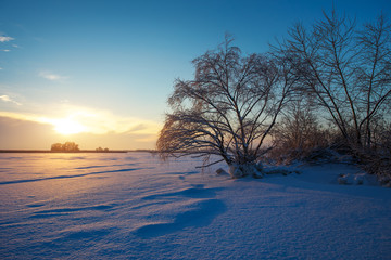 Beautiful winter landscape with frozen lake, trees and sunset sk