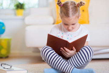 Naklejka premium Portrait of clever little girl sitting with book on the floor