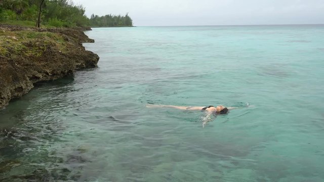 Young slender woman in black swimsuit is swimming at clear water of caribbean sea