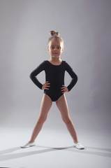 Little girl in black tights dancing on a gray background.