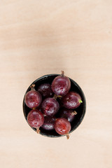 Red gooseberries in bowl on wooden table.