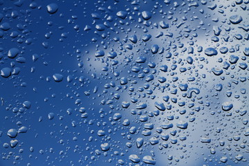 Rain drops on window with blue cloudy sky in background , spring rainy day