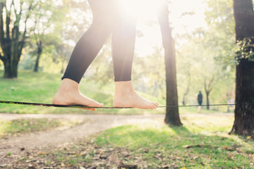 Close up on feet walking on tightrope or slackline outdoor in a city park in back light - slacklining, balance, training concept