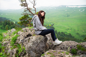 Beautiful woman sitting on mountain top and contemplating landsc