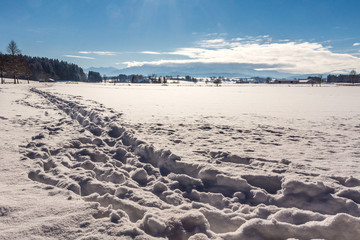 Spuren im Tiefschnee führen über ein Feld im Voralpenland