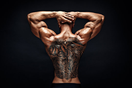 Unrecognizable muscular man with tattoo on back against of black background. Isolated.