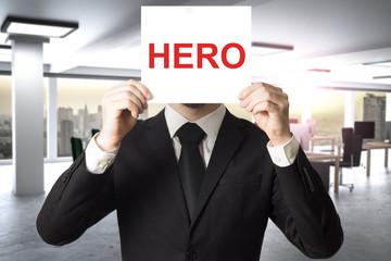 businessman in large office hiding face behind sign hero