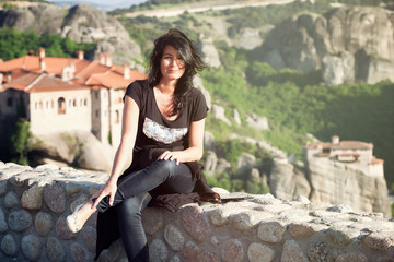 Attraktive Frau sitzt auf einer Mauer vor den Meteora Klöstern 