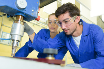 serious trainees focused on drilling metal piece with professional machinery