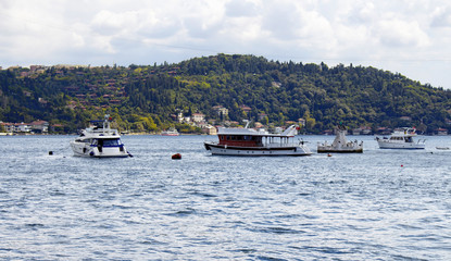 View of bay of luxury neighborhood Bebek on European side of Istanbul. Yachts, fishing boats are parked on Bosphorus. Residential buildings on Asian side are in the background. Cloudy autumn day.