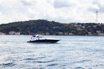 Obraz premium Luxury yacht / boat crosses Bosphorus between European and Asian sides in Istanbul. It is cloudy autumn day. It is internationally-significant waterway located in northwestern Turkey
