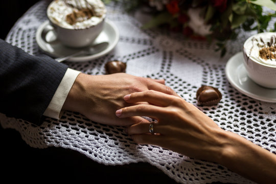couple holding hands, loving couple drinking coffee in a coffee shop, hands close-up meeting in a cafe, a beautiful bouquet,сoffee with chocolate candies