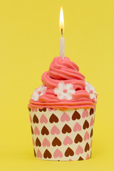 red cupcake decorated with candle on yellow background
