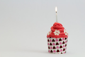 red cupcake with burning candle and sugar flowers