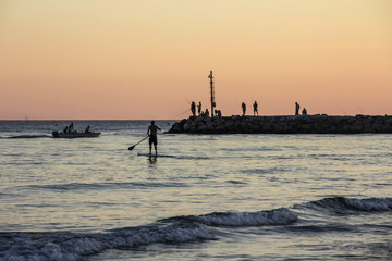 Sunset on Tyrrhenian sea, view of breakwater, SUP surfer, harbor and seacoast of Terracina, Lazio, Italy