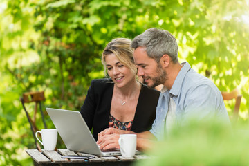 A smart couple is sitting at a terrace cafe and using a laptop