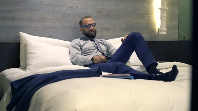 Young businessman watching TV lying on bed at night, 4k
