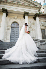 Obraz premium Wedding dress, beautiful bride in white dress with red bouquet near church-place of wedding ceremony