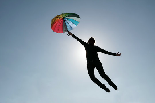 woman flying away in blue sky with rainbow colored umbrella