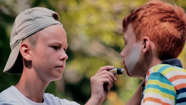 Boy is painting on the friend's face with crayon