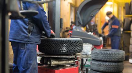 Professional auto mechanic replacing tire on wheel in car repair workshop.