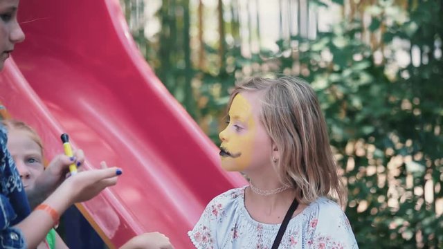 fair-haired girl is painting on the little funny girl's face
