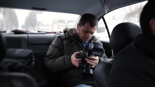A journalist traveling in a taxi with a camera in hand and check the flash operation