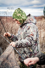 Hunter man in camouflage installing hunting tent in overcast day during hunting season