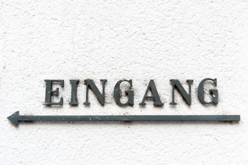 Schmiedeeisernes Hinweisschild Eingang mit Pfeil nach links an einer Hauswand, Nahaufnahme