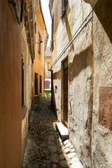 Fototapeta na wymiar Narrow path between houses. Old walls and sunlight. One way to go.